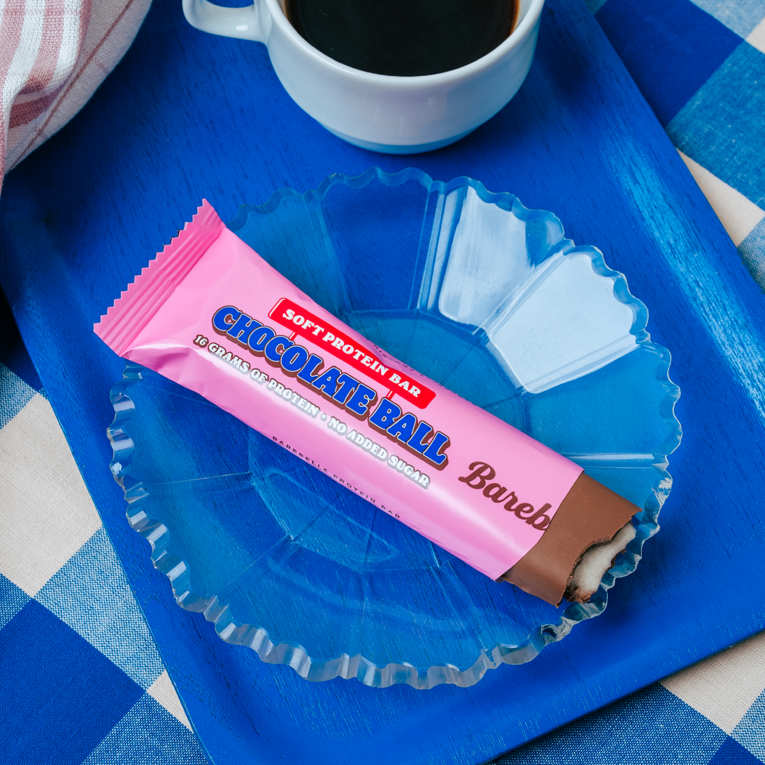 Protein bar labeled "Chocolate Ball" next to coffee on a blue tray and checkered cloth.
