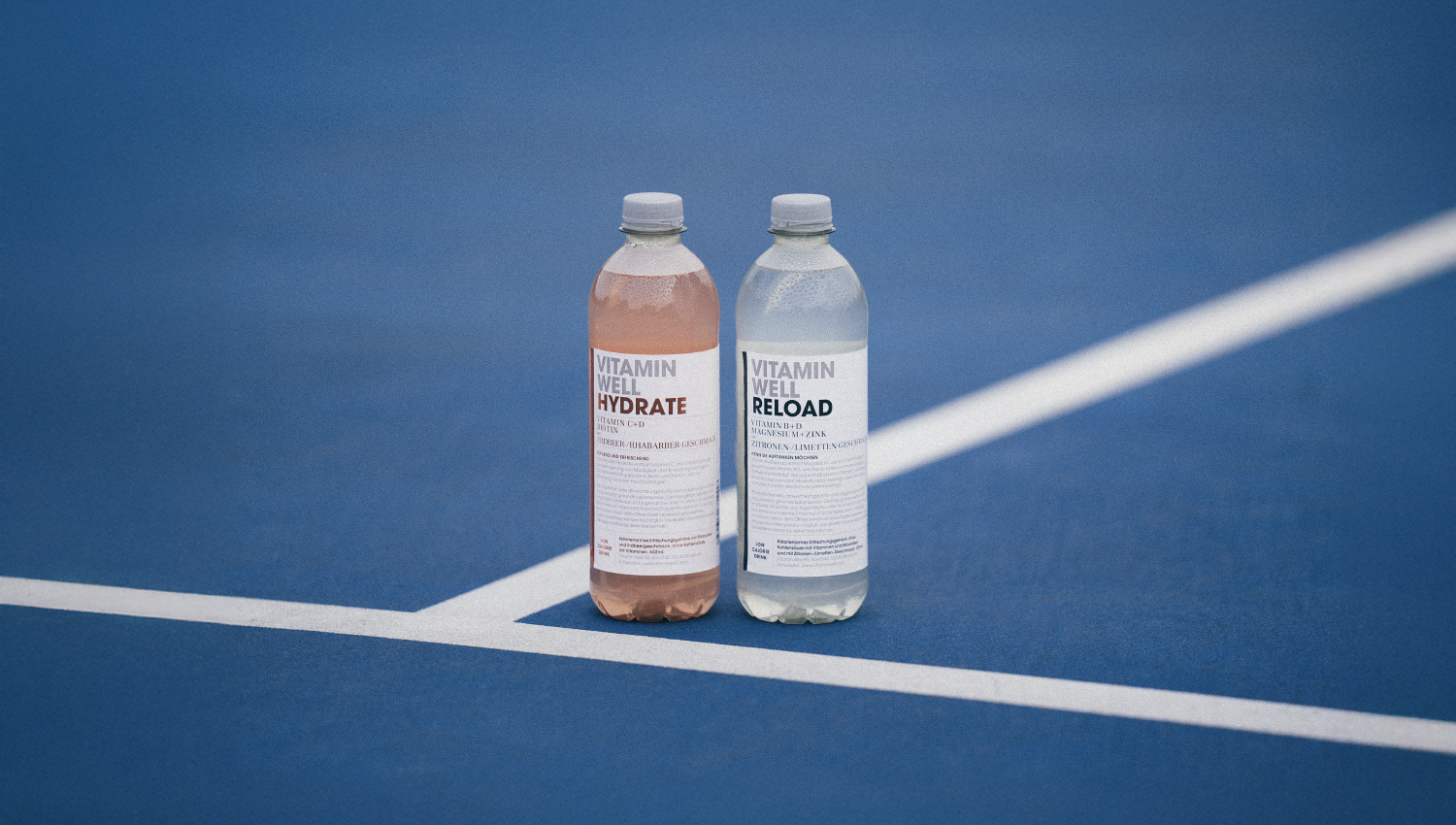 Zwei Vitaminwasserflaschen auf einem blauen Tennisplatz.