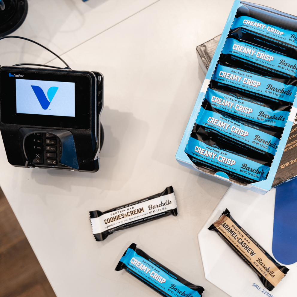 Payment terminal next to a display of Barebells protein bars on a table.