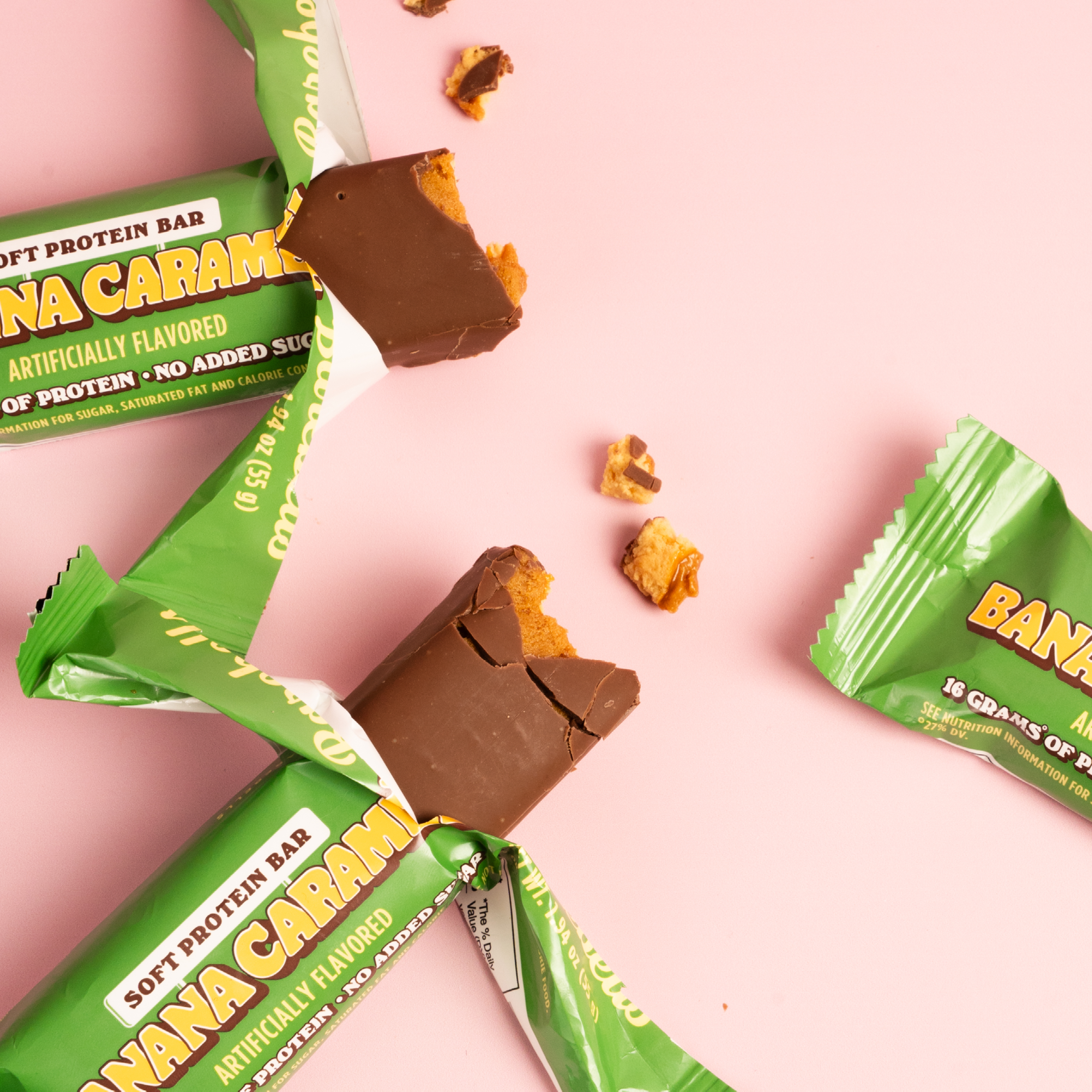 Banana caramel flavored protein bars with wrappers on a pink background.
