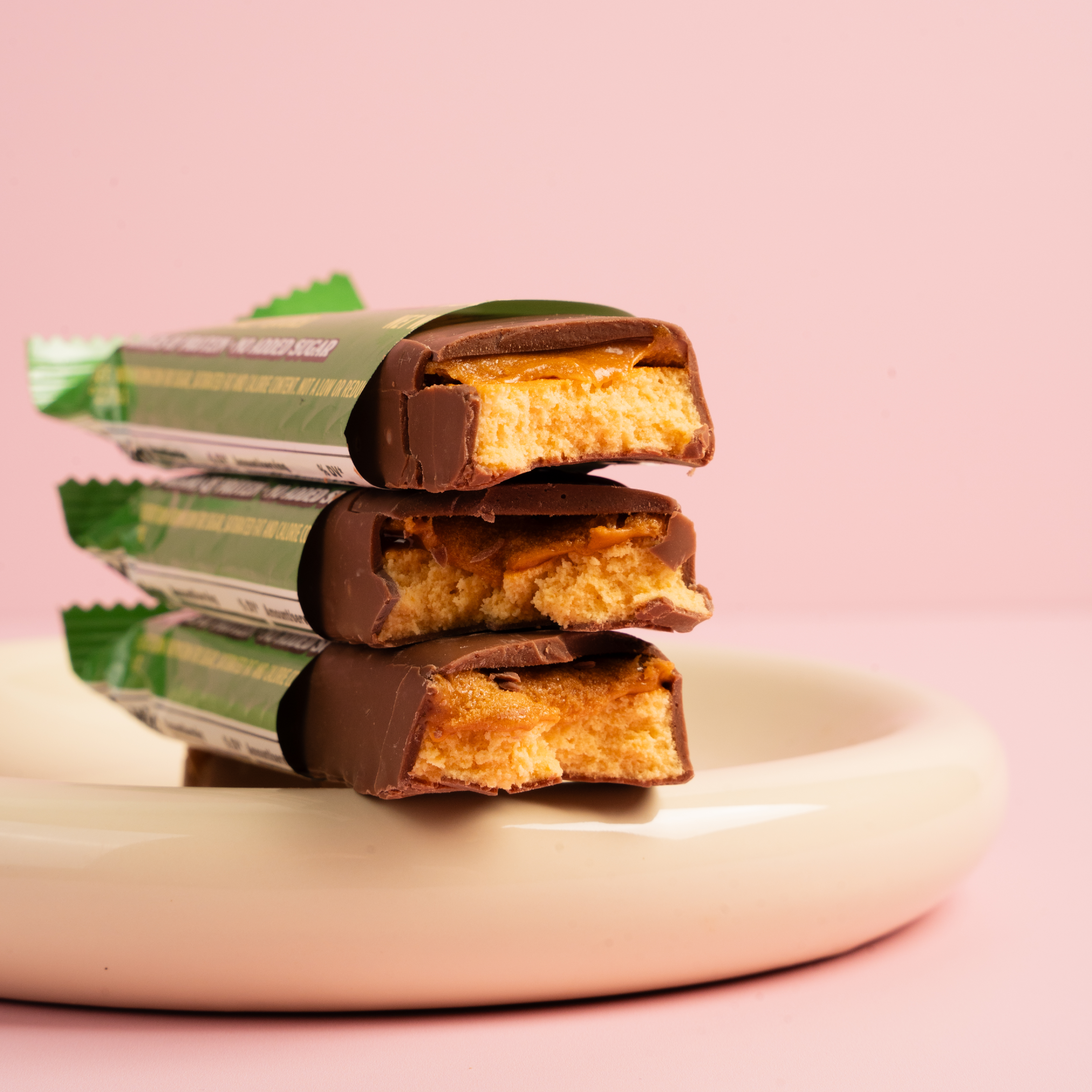 Stacked chocolate bars with caramel filling on a white plate, pink background.