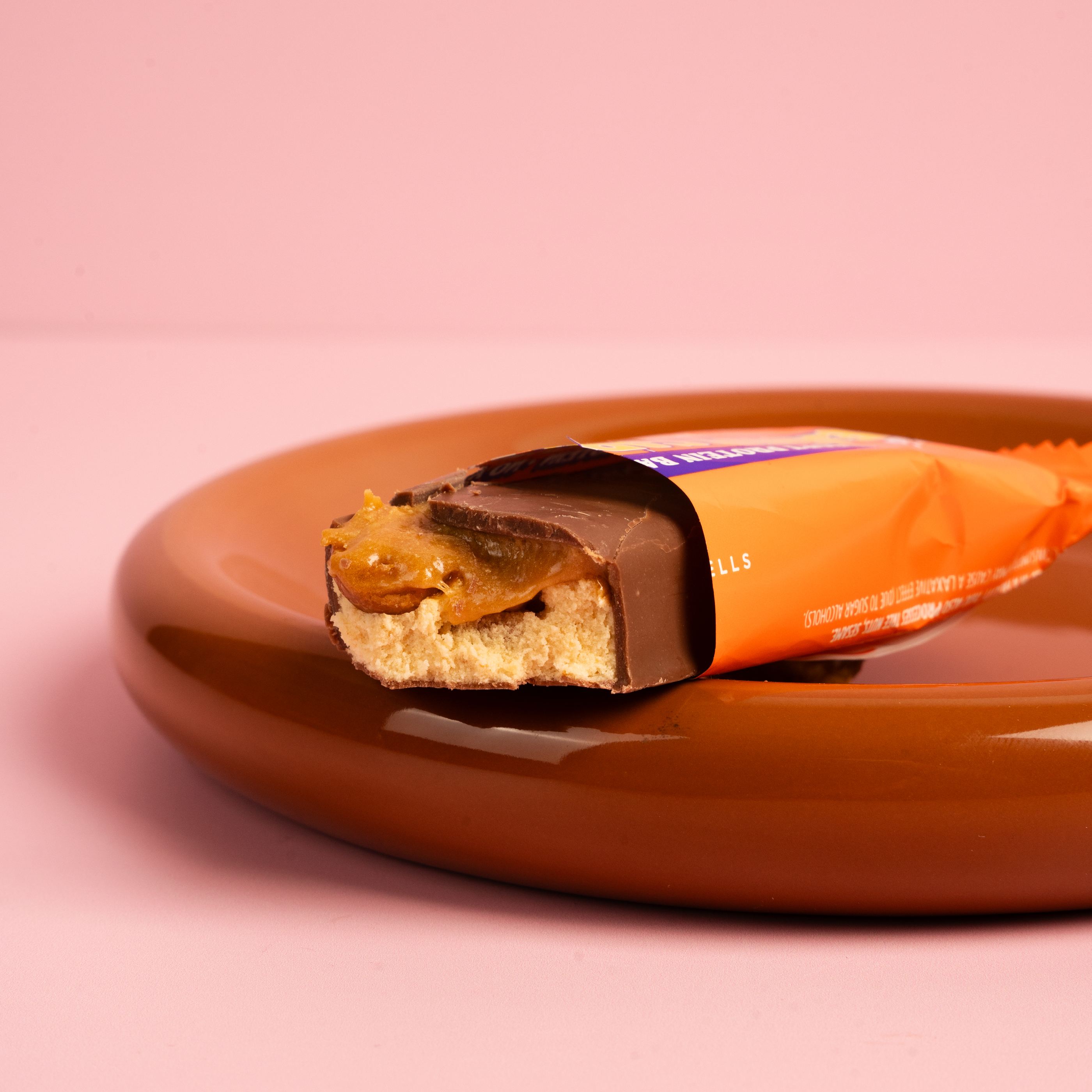 Chocolate bar with caramel on a plate, partially unwrapped.