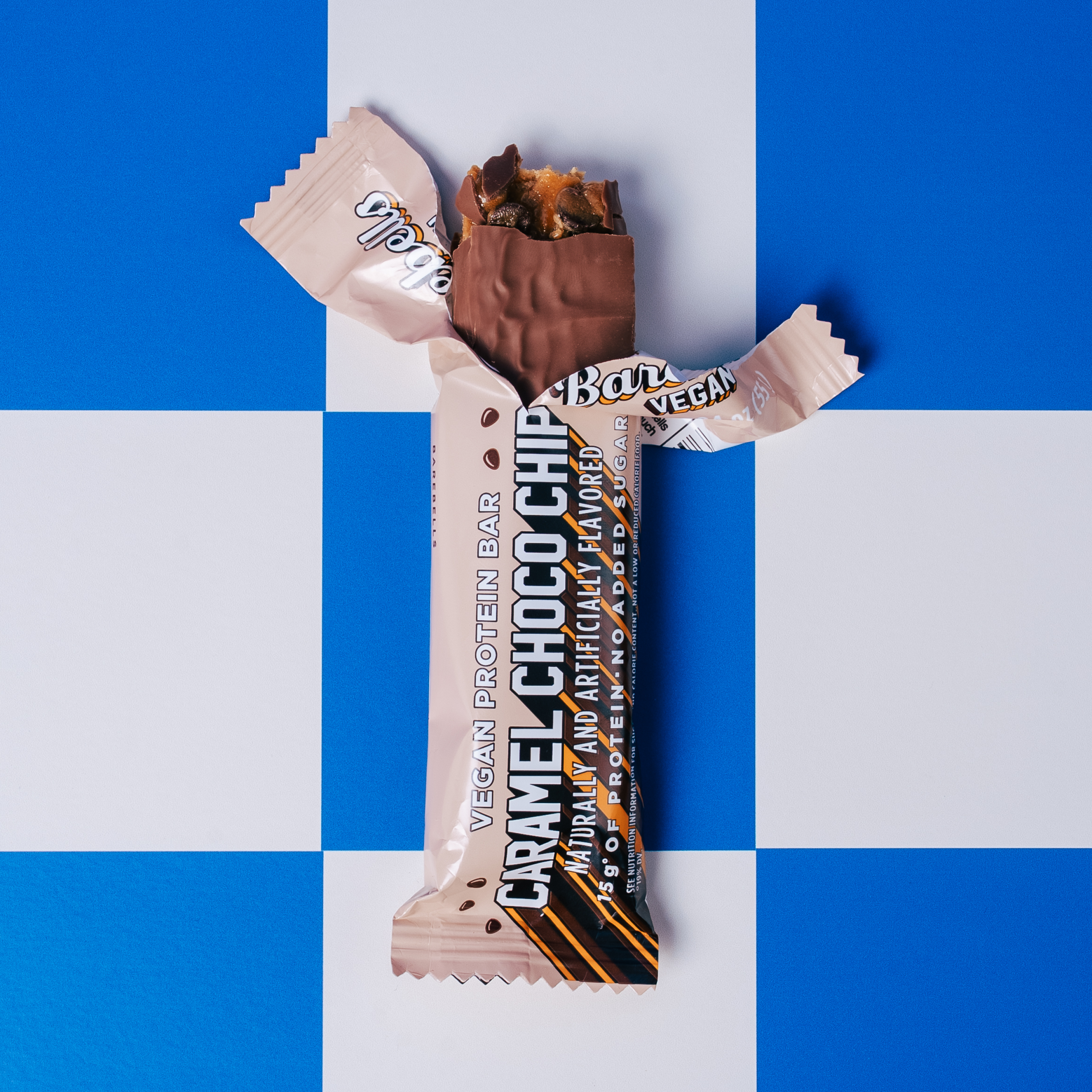 Vegan caramel choc chip protein bar partially unwrapped on a blue and white background.